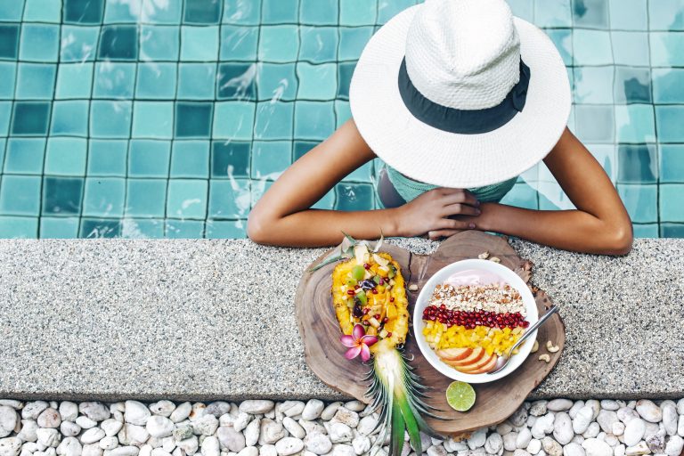 Girl,relaxing,and,eating,fruit,plate,by,the,hotel,pool.
