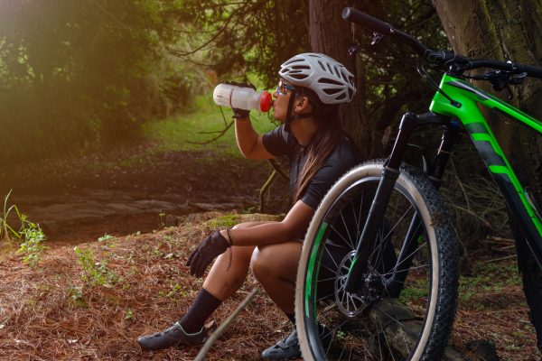Latin,woman,cyclist,sitting,drinking,water,in,the,forest,with